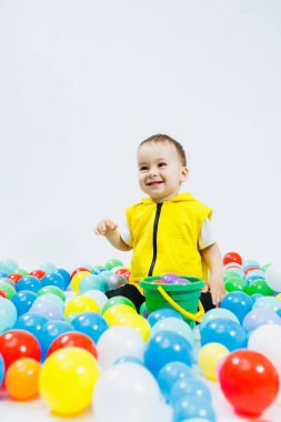 Çocuk oyun grubunda renkli toplar içinde mutlu bir çocuk. Çocuk gülümsüyor, topların arasında saklanıyor..