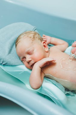 Yeni doğmuş bir bebek banyo yapmak için küvette yatıyor. Bebeği yıkıyorum. Yeni doğanların ve çocukların hijyeni.