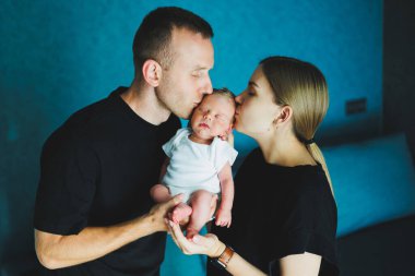 Mutlu anne ve baba yeni doğmuş bebeklerini kollarında tutuyorlar. Genç anne ve baba yeni doğmuş bebeğe sarılıyor. Evde genç bir aile ve yeni doğmuş bir bebek.