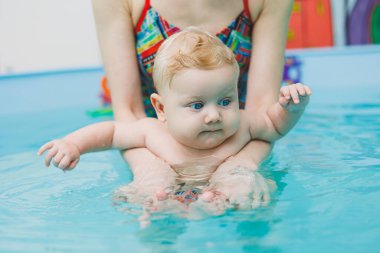Bir bebek bir antrenörle havuzda yüzmeyi öğrenir. Bebek yüzmeyi öğreniyor. Çocuk gelişimi.