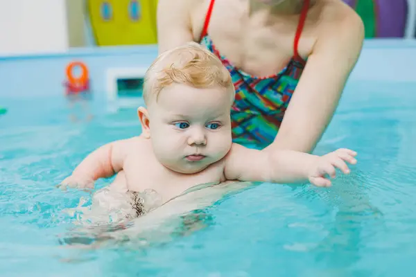 A baby learns to swim in a pool with a trainer. Baby learning to swim. Child development.