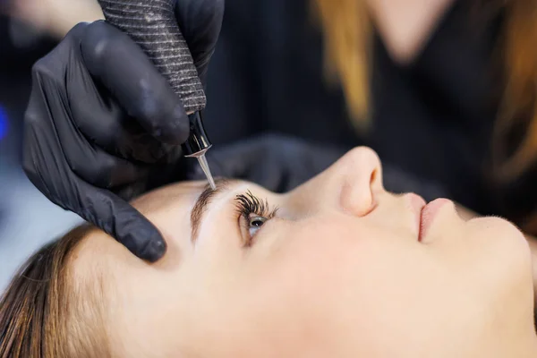 Permanent make-up of eyebrows. Woman professional permanent make-up artist with a permanent make-up tool. A young permanent makeup artist makes permanent eyebrow makeup