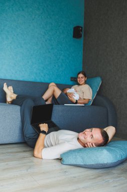 Bebekli aileler evdeki kanepede dizüstü bilgisayarlarıyla oturup internette konuşuyorlar. Çocuklu genç bir aile evde kanepede otururken dizüstü bilgisayarda çalışıyor..