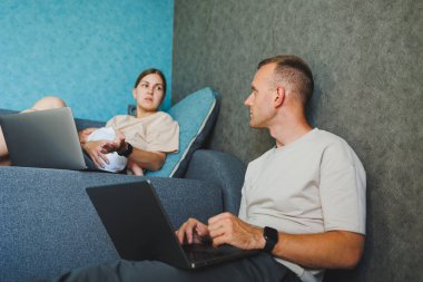 Bebekli aileler evdeki kanepede dizüstü bilgisayarlarıyla oturup internette konuşuyorlar. Çocuklu genç bir aile evde kanepede otururken dizüstü bilgisayarda çalışıyor..