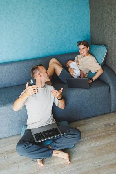 stock image Smiling mom working at home with her child on the sofa while writing an email. Young woman working from home, while in quarantine isolation during the Covid-19 health crisis