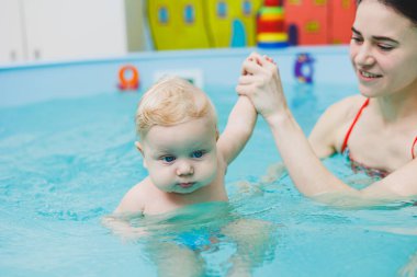 5 aylık bir bebek bir koçla havuzda yüzmeyi öğrenir. Bebek yüzmeyi öğreniyor.