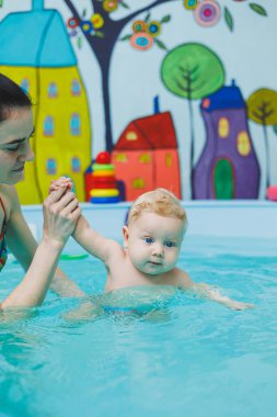 5 aylık bir bebek bir koçla havuzda yüzmeyi öğrenir. Bebek yüzmeyi öğreniyor.