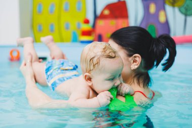 Çocuklara yüzmeyi öğretmek. Bir bebek bir antrenörle havuzda yüzmeyi öğrenir. Bebek yüzmeyi öğreniyor. Çocuk gelişimi.
