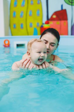 Çocuklara yüzmeyi öğretmek. Bir bebek bir antrenörle havuzda yüzmeyi öğrenir. Bebek yüzmeyi öğreniyor. Çocuk gelişimi.