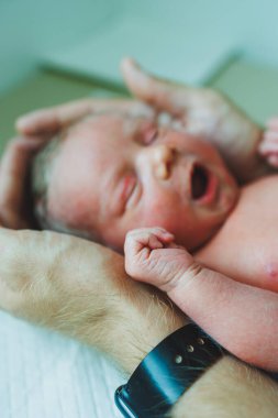 Yeni doğmuş erkek bebek babasının kollarında, kollarının üstünde uzanmış, yakından bakıyor. Bir adam kucağında küçük bir çocuk tutuyor. Sağlıklı yaşam tarzı. Babalık