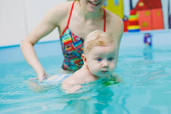 A 5-month-old baby learns to swim in a pool with a coach. Baby learning to swim.