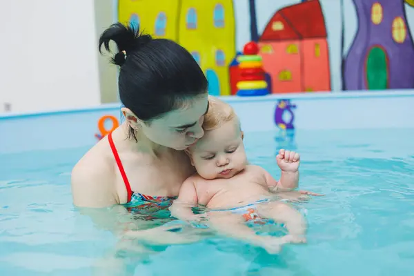 A 5-month-old baby learns to swim in a pool with a coach. Baby learning to swim.