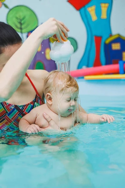A baby learns to swim in a pool with a trainer. Baby learning to swim. Child development.