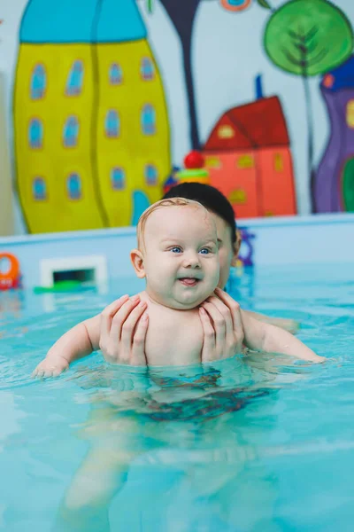 A newborn baby swims in the pool. Teaching children to swim. A baby learns to swim in a pool with a trainer. Baby learning to swim. Child development.