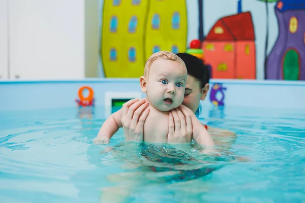 A newborn baby swims in the pool. Teaching children to swim. A baby learns to swim in a pool with a trainer. Baby learning to swim. Child development.