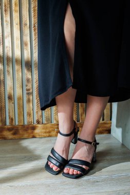 Siyah deri sandaletlerle ince kadın bacakları. Yazlık kadın ayakkabıları koleksiyonu. Yaz için şık kadın ayakkabıları. Kadınların ayaklarında kadın sandaletleri