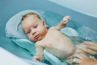 İki aylık bir bebeği küvette yıkarken, çocuk plastik bir tezgahta yatıyor. Bebek bakımı.