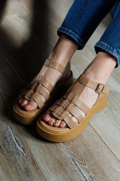Beige leather sandals on women\'s feet. Female feet in comfortable casual sandals