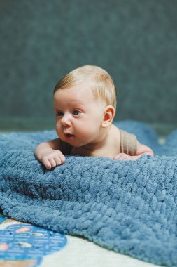 A small newborn boy lies on a gray knitted blanket. Portrait of a one-month-old baby