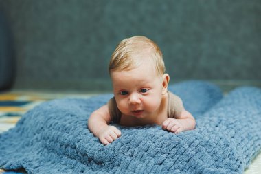 A small newborn boy lies on a gray knitted blanket. Portrait of a one-month-old baby