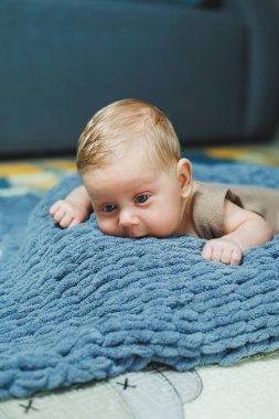 A small newborn boy lies on a gray knitted blanket. Portrait of a one-month-old baby