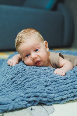 Photo of a baby in a knitted overall. A small newborn boy lies on a gray knitted blanket. Portrait of a one-month-old baby