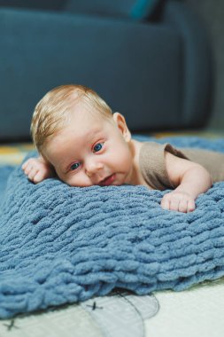 Photo of a baby in a knitted overall. A small newborn boy lies on a gray knitted blanket. Portrait of a one-month-old baby