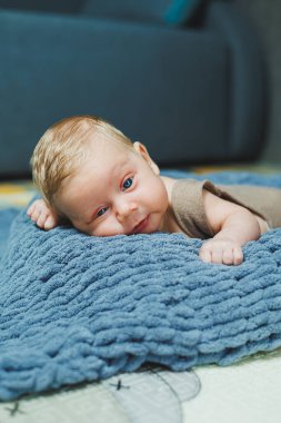 Photo of a baby in a knitted overall. A small newborn boy lies on a gray knitted blanket. Portrait of a one-month-old baby
