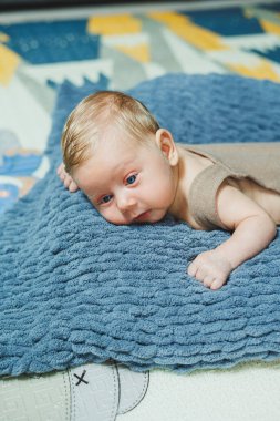 Photo of a baby in a knitted overall. A small newborn boy lies on a gray knitted blanket. Portrait of a one-month-old baby