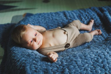 Photo of a baby in a knitted overall. A small newborn boy lies on a gray knitted blanket. Portrait of a one-month-old baby