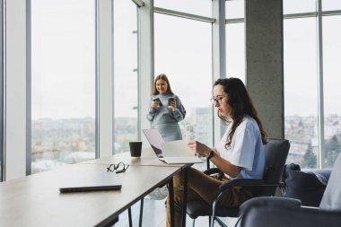 İki genç kadın modern bir ofiste çalışıyor. Büyük pencereli çalışma odası. Kadın yönetici ofiste oturan masada çalışıyor..