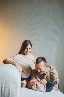 Yeni doğmuş bebekleri olan genç ve mutlu ebeveynler evlerinde kanepede. Beyaz bir arka planda yeni doğmuş bebekleri olan anne ve baba.