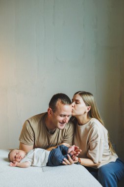 Yeni doğmuş bir bebeği olan genç bir aile. Mutlu anne ve baba çocuklarını öpüyor. Ebeveynler ve kollarında gülümseyen bir çocuk.