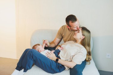 Yeni doğmuş bir bebeği olan genç bir aile. Mutlu anne ve baba çocuklarını öpüyor. Ebeveynler ve kollarında gülümseyen bir çocuk.