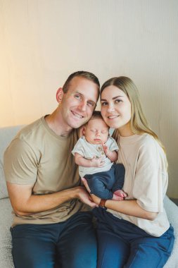 Yeni doğmuş bebekleri olan genç ve mutlu ebeveynler evlerinde kanepede. Beyaz bir arka planda yeni doğmuş bebekleri olan anne ve baba.