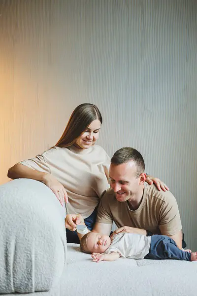 Yeni doğmuş bir bebeği olan genç bir aile. Mutlu anne ve baba çocuklarını öpüyor. Ebeveynler ve kollarında gülümseyen bir çocuk.