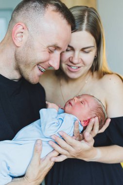 Mutlu genç ebeveynler yeni doğan oğullarını kollarında tutuyorlar. Gülümseyen mutlu çift yeni doğan bebeklerine sarılıyor. Yeni doğmuş bir bebek için bir gün.