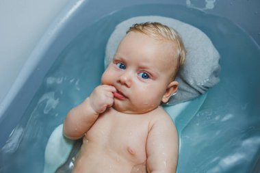 4 aylık küçük bir çocuk, küvette küvette ayakta yatarken banyo yapıyor. Yeni doğmuş bir bebeğe bakmak, bebeği yıkamak.