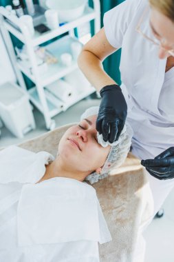 Masaj masasında oturan, genç bir kadının yüzüne masaj yapan ve yüz bakımı yapan kadın hastalarla birlikte çalışan bir dermatolog ya da kozmetikçinin ofisi. Yüz bakımı.