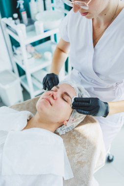 Masaj masasında oturan, genç bir kadının yüzüne masaj yapan ve yüz bakımı yapan kadın hastalarla birlikte çalışan bir dermatolog ya da kozmetikçinin ofisi. Yüz bakımı.