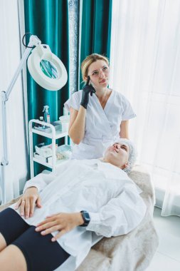 Gülümseyen bir kozmetik uzmanı hastasına güzellik ameliyatı yapıyor. Yüz bakımı. Kozmetoloji ve dermatoloji.
