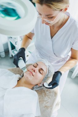 Klinikteki bir cildiyeci ya da kozmetikçi kadın hastalarla çalışır ve genç bir kadının yüzünde yüz bakımı yapar. Kozmetik uzmanının ofisindeki yüz ultrasonik temizleme.