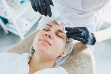 Klinikteki bir cildiyeci ya da kozmetikçi kadın hastalarla çalışır ve genç bir kadının yüzünde yüz bakımı yapar. Kozmetik uzmanının ofisindeki yüz ultrasonik temizleme.