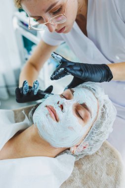 Güzellik uzmanının ofisi bir kaplıca salonundaki bir kadının yüzüne maske takıyor, yukarısı manzaralı. Estetik prosedür. Yüz derisi için bakım maskesi.