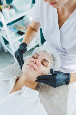 Güzellik uzmanının ofisi bir kaplıca salonundaki bir kadının yüzüne maske takıyor, yukarısı manzaralı. Estetik prosedür. Yüz derisi için bakım maskesi.