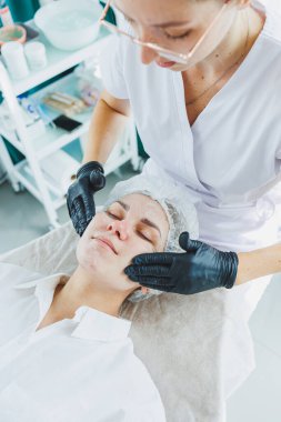 Güzellik uzmanının ofisi bir kaplıca salonundaki bir kadının yüzüne maske takıyor, yukarısı manzaralı. Estetik prosedür. Yüz derisi için bakım maskesi.