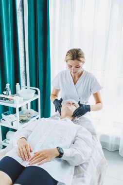 Güzellik uzmanının ofisi bir kaplıca salonundaki bir kadının yüzüne maske takıyor, yukarısı manzaralı. Estetik prosedür. Yüz derisi için bakım maskesi.