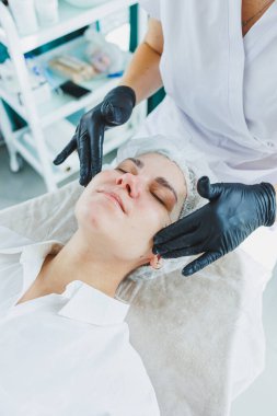 Güzellik uzmanının ofisi bir kaplıca salonundaki bir kadının yüzüne maske takıyor, yukarısı manzaralı. Estetik prosedür. Yüz derisi için bakım maskesi.