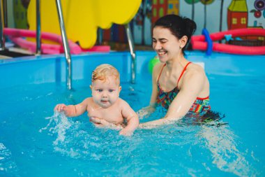 Havuzda yüzen bir bebek. Yeni doğmuş bir çocuğa koçla havuzda yüzmeyi öğretmek.