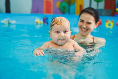 Havuzda yüzen bir bebek. Yeni doğmuş bir çocuğa koçla havuzda yüzmeyi öğretmek.